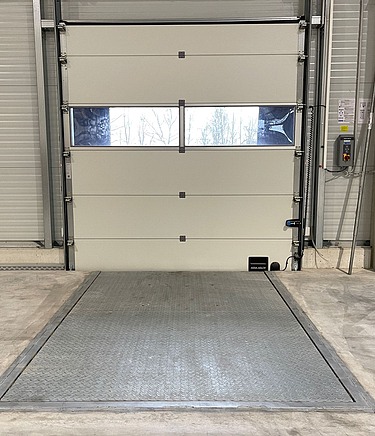 Industrie-Laderampe aus Beton vor geschlossenem Sektionaltor in moderner Logistikhalle – robuste Metallplattform für effiziente Be- und Entladung von LKWs, ideal für Lager- und Versandprozesse.