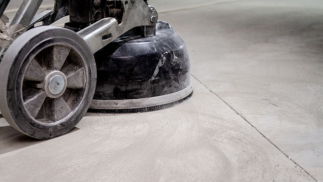 Boden-Schleifmaschine beim Schleifen einer Betonoberfläche. Auf dem Boden sind kreisförmige Schleifspuren und Staubrückstände zu sehen, die vom Arbeitsvorgang stammen.