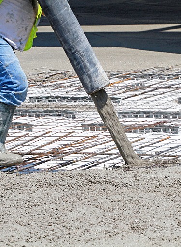 Ein Bauarbeiter bringt frischen Beton auf eine Stahlarmierung auf, um einen widerstandsfähigen Industrieboden zu erstellen. Der Beton wird gleichmäßig verteilt, um eine hygienische, belastbare und langlebige Bodenfläche zu gewährleisten