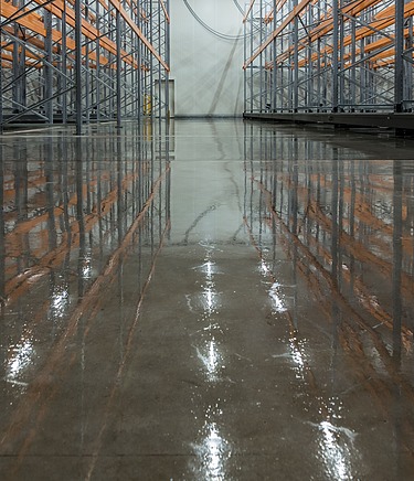 Industriehalle mit glänzend poliertem Betonboden und Metallregalen – professionelle Oberflächenveredelung für langlebige, pflegeleichte und ästhetische Böden in Lager- und Produktionsbereichen.