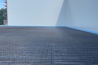 Bewehrte Betonbodenfläche mit dicht verlegter Stahlarmierung in einer modernen Industriehalle vor dem Betonieren, großflächiger Rohbau mit hellen Betonwänden und blauem Himmel