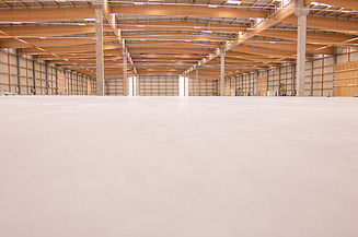 Betonboden in überdachter heller Halle. Betonpfeiler stützen das Dach.