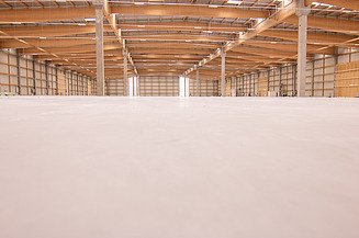 Betonboden in überdachter heller Halle. Betonpfeiler stützen das Dach.