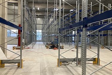  Industrielle Lagerhalle mit neu montierten Hochregalen aus Stahl, breiten Gängen und Betonboden – modernes Lager- und Regalsystem für Logistik, Gefahrstofflager oder Industrie.