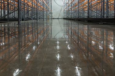 Industriehalle mit glänzend poliertem Betonboden und Metallregalen – professionelle Oberflächenveredelung für langlebige, pflegeleichte und ästhetische Böden in Lager- und Produktionsbereichen.