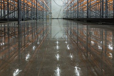 Industriehalle mit glänzend poliertem Betonboden und Metallregalen – professionelle Oberflächenveredelung für langlebige, pflegeleichte und ästhetische Böden in Lager- und Produktionsbereichen.