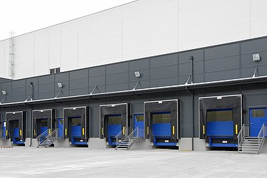 Mehrere moderne Laderampen an der Rückseite eines großen Industrie- oder Logistikgebäudes. Vor den Rampen befindet sich eine breite, saubere Betonfläche, die als Lade- und Rangierbereich für Lkw dient.