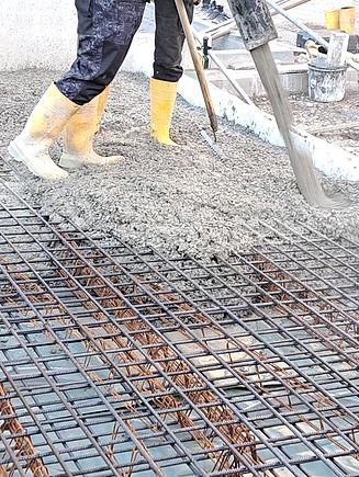 Beton wird auf eine Bewehrung aus Stahl gegossen, Bauarbeiter mit gelben Gummistiefeln verteilt Frischbeton auf einer Baustelle. Betonarbeiten für Fundamentbau und Stahlbeton-Konstruktionen