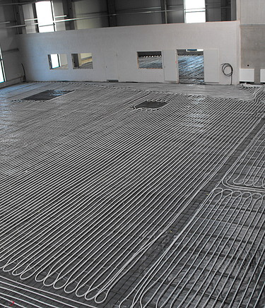 Nahaufnahme einer Industrieflächenheizung mit weißen Kunststoffrohren in Serpentinenform, befestigt auf einem markierten Verlegegitter.