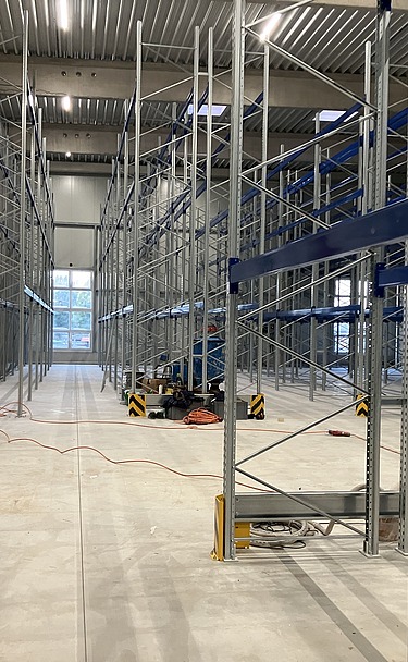 Industrielle Lagerhalle mit neu montierten Hochregalen aus Stahl, breiten Gängen und Betonboden – modernes Lager- und Regalsystem für Logistik, Gefahrstofflager oder Industrie.