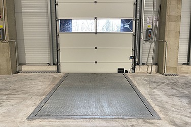 Industrie-Laderampe aus Beton vor geschlossenem Sektionaltor in moderner Logistikhalle – robuste Metallplattform für effiziente Be- und Entladung von LKWs, ideal für Lager- und Versandprozesse.