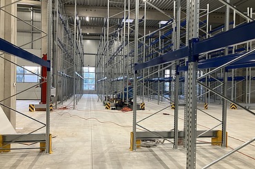 Industrielle Lagerhalle mit neu montierten Hochregalen aus Stahl, breiten Gängen und Betonboden – modernes Lager- und Regalsystem für Logistik, Gefahrstofflager oder Industrie.