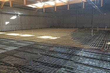 Vorbereitung für eine Betonbodenplatte in einer Industriehalle: Bewehrungsstahl und Rohrleitungen für Fußbodenheizung vor dem Betonieren.